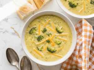 Creamy Broccoli Cheddar Soup served in white bowl with fresh broccoli florets and melted cheese on top