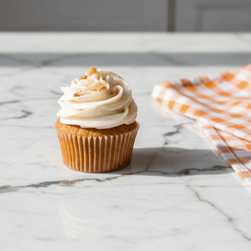 Carrot Cake Cupcakes topped with cream cheese frosting and walnut garnish on white plate