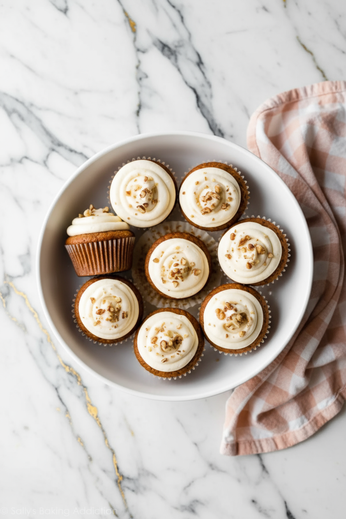 Carrot Cake Cupcakes topped with cream cheese frosting and walnut garnish on white plate