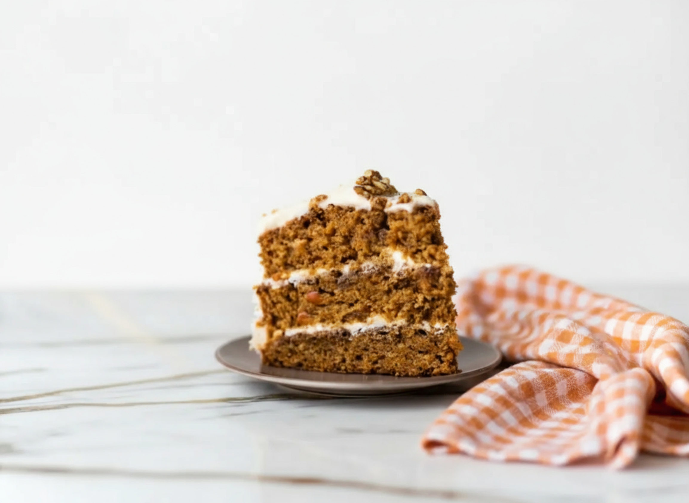 Carrot Cake with Candied Pecans topped with cream cheese frosting and caramelized pecan pieces on a white plate