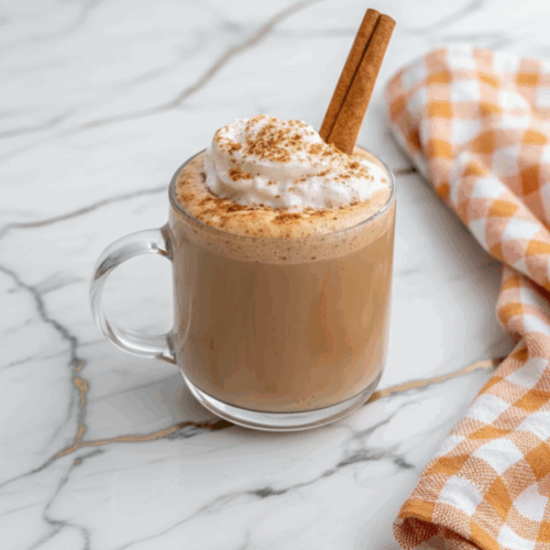 Homemade Pumpkin Spice Latte topped with whipped cream and cinnamon in a clear glass mug on a rustic wooden table