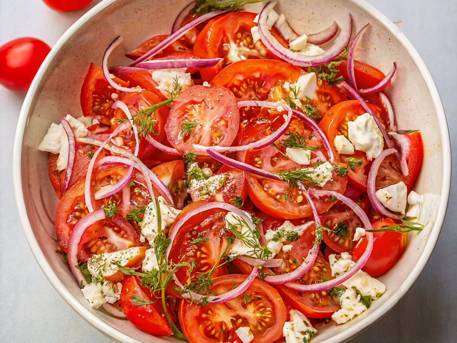 Tomato Salad with fresh cherry tomatoes, basil leaves, and dressing in a white bowl