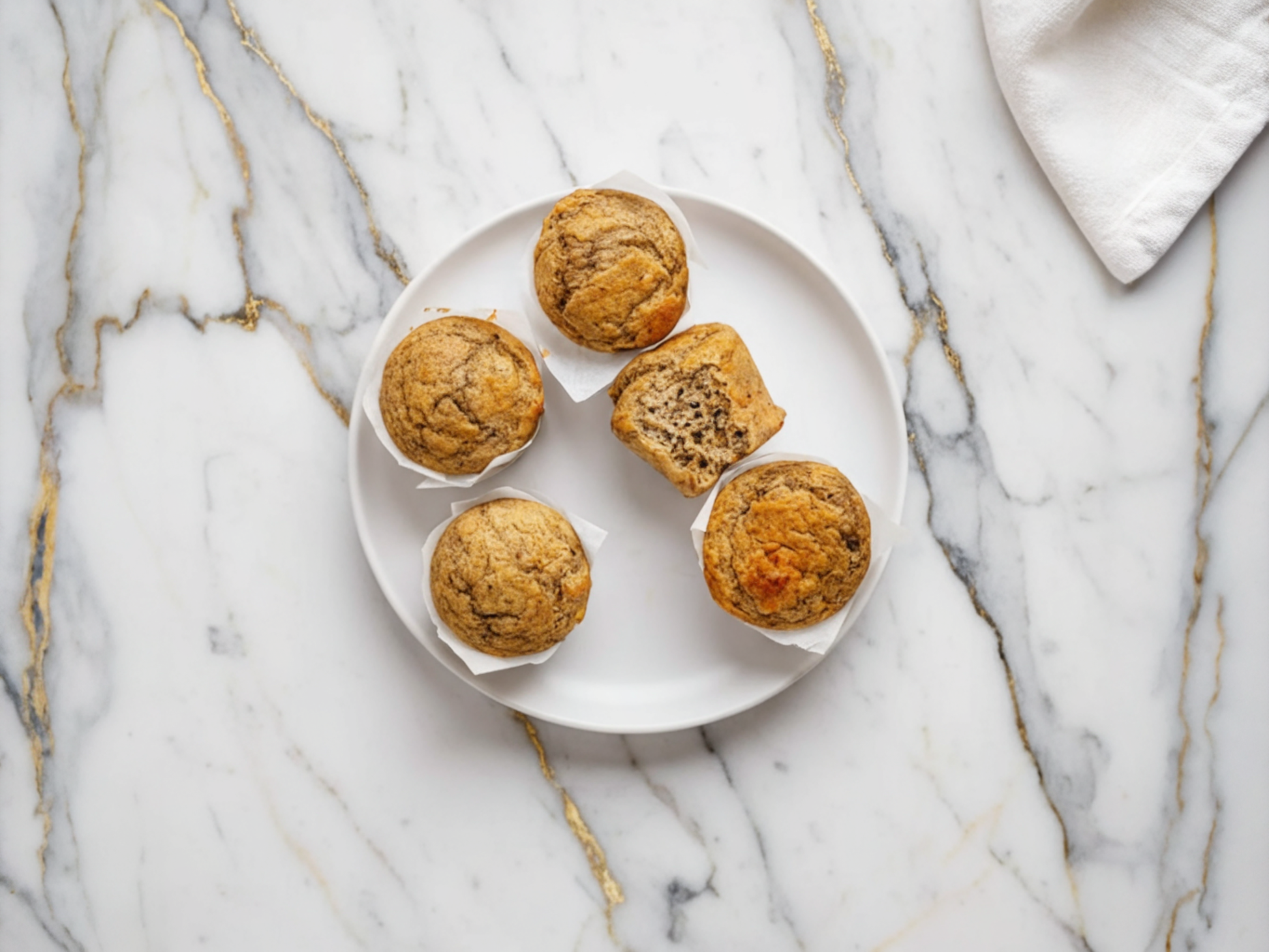 Banana Cottage Cheese Muffins with golden tops arranged on a white plate with fresh banana slices