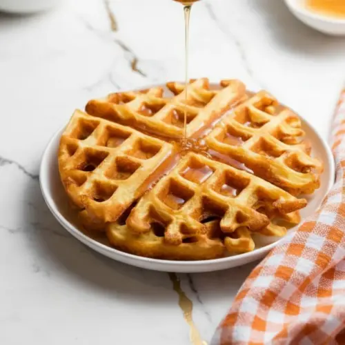 Golden brown cottage cheese chaffle on a plate with butter and fresh berries on top