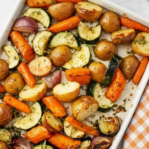 Garlic herb roasted potatoes carrots and zucchini arranged on a baking sheet with golden brown edges and fresh herbs