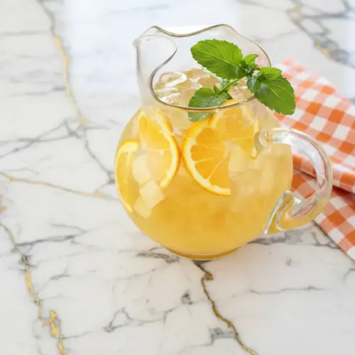 Snowy pineapple punch served in a glass pitcher with ice and fresh pineapple garnish
