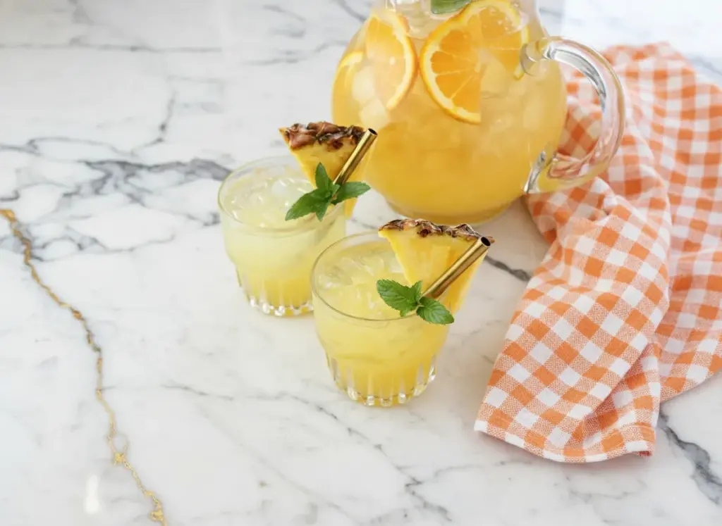 Snowy pineapple punch served in a glass pitcher with ice and fresh pineapple garnish